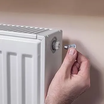 Technicien effectuant la purge manuelle d'un radiateur avec une clé de purge